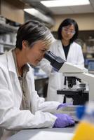 Focused scientist using microscope in lab. Two researchers in lab coats photo