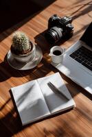 Workspace with notebook, laptop, camera, and cactus photo