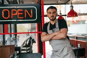 Standing with arms crossed, shop is opened. Man is serving delicious street food photo