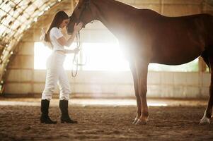 Side view,,, embracing the animal. Beautiful young woman is with horse indoors photo