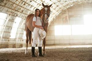 Daylight ,comes through the ,windows. Beautiful young woman is with horse indoors photo