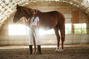 Standing, and, posing. Beautiful young woman is with horse indoors photo