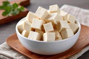 Bowl of diced tofu cubes on wooden board with parsley sprig photo