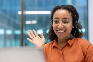 A cheerful customer service representative waves while wearing a headset in her office. She is smiling, and looking forward. photo