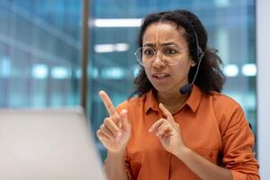 An african american woman gestures with hands during a call, likely discussing a business issue with a serious expression while at the office. photo