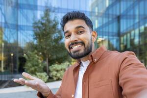 An enthusiastic man gestures while smiling during an outdoor call near a modern building photo