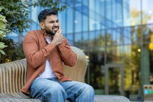 A man with a pained expression clutches his jaw, clearly suffering from a toothache while sitting on a bench. photo