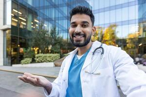 A cheerful doctor gestures towards the viewer, inviting or presenting, in front of a modern glass building. photo