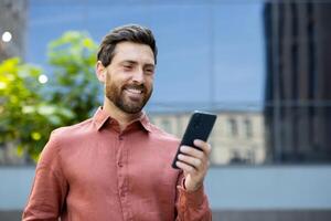 A man smiles while looking at his phone in an urban setting. He appears pleased with what he sees on the mobile device. photo