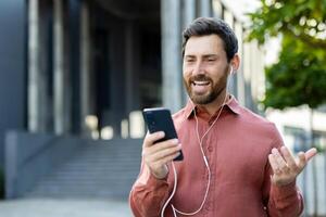 A man in a red shirt is having a call while outside of a building. He is smiling and gesturing. photo