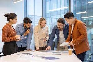 A diverse group of professionals collaborate around a table, reviewing documents and planning strategies in the office setting. photo