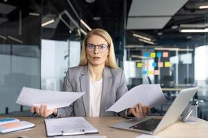 A professional woman appears perplexed while holding documents in a modern office setting. She seems surprised with the information. photo