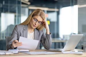 A focused businesswoman, engrossed in the details of paperwork, working in a modern, open office setting with a laptop. photo