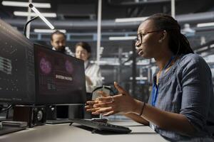 Scared admin in data center panicked by virus alert, initiating protocol to protect critical systems. African American woman in server room assessing compromised gear after hacker attack photo