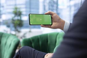 Young leader in the office looks at green screen on his smartphone and analyzes financial data, setting company objectives and implementing strategic planning for long term business success. photo