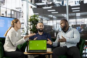 Isolated screen notebook next to multiethnic team working in office, coordinating company administrative operation. Diverse coworkers reviewing business data metrics on chroma key laptop photo