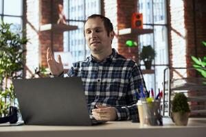 home office employee looking at laptop screen, saluting colleagues during online videocall. Businessperson in home office greeting team members during videoconference meeting on notebook photo