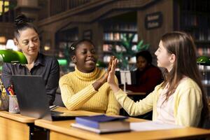 Cheerful diverse classmates sharing a high five during private lessons with tutor in the library, finishing their team project work. Elementary school pupils feeling satisfied with academic progress. photo