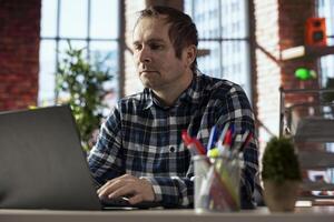 Freelancer in home office using laptop, checking emails displayed on screen, reading messages in inbox. Teleworker in apartment workspace managing electronic correspondence on notebook photo