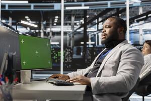 Server hub engineer looking at data visualization on green screen PC to pinpoint equipment performance issues. Data center worker looks at analysis graph on chroma key computer to reduce failures photo