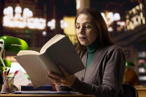 Mature female student in a work room surrounded by books and documents, preparing for a master dissertation and researching academic materials at the campus library. Higher education. photo