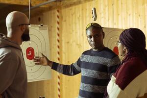 Shooting range safety specialist ensuring clients are operating weapons safely, explaining gun holding etiquette. Firing range gallery worker discusses rules with clients, teaching how to use firearms photo