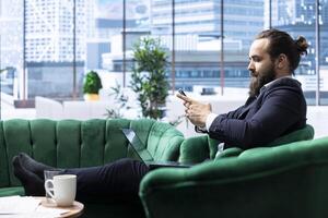 Motivated boss working tirelessly in a high end downtown workspace, reviewing financial forecasts and tracking sales performance. Chief executive officer scrolls smartphone with authority. photo