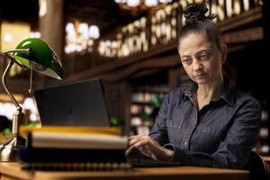 Professional author and librarian working on her laptop in a public library, focused on providing academic resources and guidance. Evaluating educational information within the database. photo