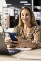 General manager uses her smartphone to browse social media and check emails, taking a small break from office tasks. CEO using mobile technology to stay on top of management operations. photo