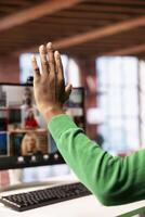 Teleworker at home office desk raising hand to request turn to speak during online videocall on PC. Close up of remote employee in apartment greeting team members during videoconference meeting photo