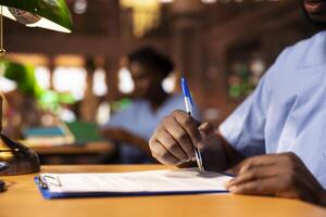 African american medical scholar creates a summary of class notes to learn easily for an exam, collecting information from the library to complete his knowledge. Future medic at desk. Close up. photo