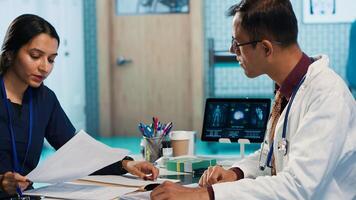 General practitioner consulting patient and reviewing x ray test results, utilizing technology for an analysis and patient care management in a medical environment. Healthcare provider. Camera A. photo