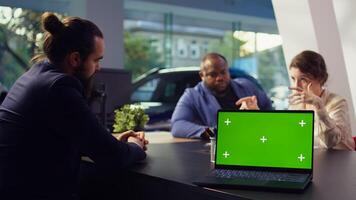 Dealership salesperson looking over appointment list on green screen laptop spreadsheet to schedule car test drive for customers. Showroom agent organizing test drive using mockup notebook, camera B photo