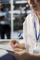 Woman in data center taking note on fixes to be made after running diagnostic scripts on computer. Server room admin writing repairing needed by supercomputers after evaluating performance metrics photo