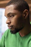 Close up side profile shot of young man with contemplative look doing tasks in apartment. African american person with focused expression looking at something, close up shot photo
