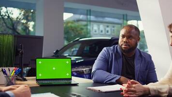 Salesman using isolated screen laptop to present car addons options to clients, trying to sway them to make purchase. Showroom agent offers warranty to customers, holding chroma key notebook, camera B photo