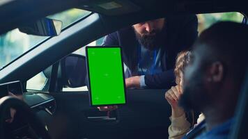 Showroom salesman showing stat charts on green screen tablet to clients after test drive. Dealership agent showing vehicle driving metrics graphs on chroma key device to couple, camera A photo