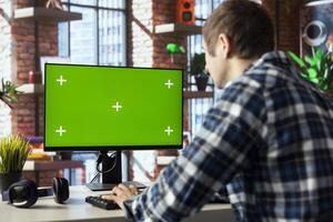 Teleworker in home office using chroma key computer display to answer emails from business associates. Man typing on green screen device keyboard, solving tasks in apartment photo