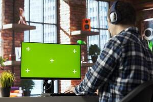 Freelancer listening music, analyzing data on isolated screen PC monitor at desk, compiling analytical reports. Employee wearing headphones using chroma key computer display, finishing project photo