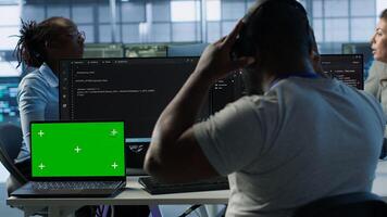 Isolated screen laptop next to programmer coding in server farm while listening music in headphones. Worker safeguarding hardware against unauthorized access with chroma key notebook, camera A photo