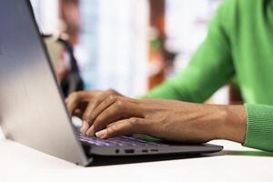 Remote employee seated at home office desk using notebook, checking emails displayed on screen, reading messages in inbox. Close up of teleworker managing electronic correspondence, typing on keyboard photo