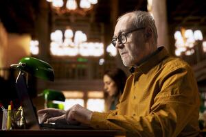 Elderly adult reading complex research documents under a green lamp, showcasing the power of wisdom and focus in senior learning environments. Academic studying in a public library. photo