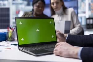 Factory employee works on green screen laptop next to executives discussing solar panel automation strategies. Worker typing on mockup notebook next to team enhancing manufacturing processes, Close up photo