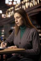 Adult woman studies alone in a library and transcribing a lecture, concentrating on paperwork and showing her commitment to researching. Pupil preparing for her college thesis. photo