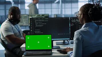 Diverse team of developers in server hub using green screen laptop, looking for misconfigurations. African american IT experts mending data center bugs with chroma key notebook, camera A photo