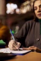 Adult learner transcribes information during a lecture in a university library, surrounded by academic textbooks and archived documents. Higher education personal goals on campus. Close up. photo
