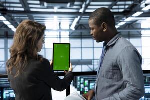 Team of technician in data center using green screen mockup tablet, adjusting power management settings. Coworkers in server room optimizing resource utilization with chroma key device photo
