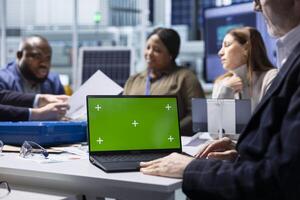 Shareholders and production plant manager analyzing sustainable manufacturing data using green screen laptop. Investors review documentation on chroma key notebook to evaluate investment profitability photo