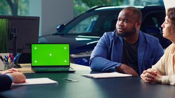 Dealership salesman showing car models on isolated screen laptop to clients, making recommendations. Showroom agent presents financing options to customers on mockup notebook, camera A photo