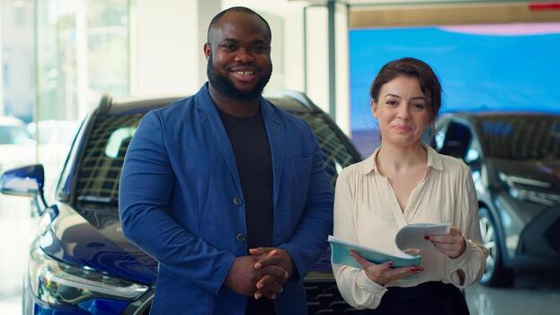 Portrait of happy customers in car showroom browsing automobiles catalog, checking characteristics and features before taking test drive. Cheerful clients comparing vehicle models, camera A photo